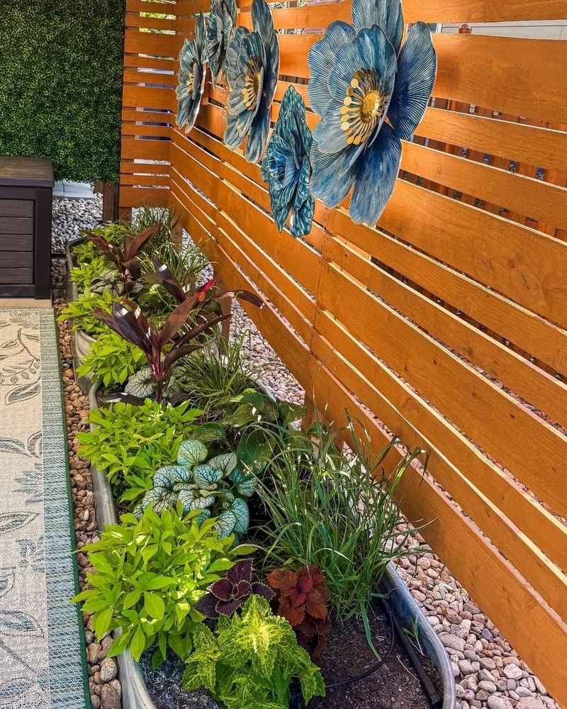 Cedar slat fence with blue metal flower art above a long planter bed