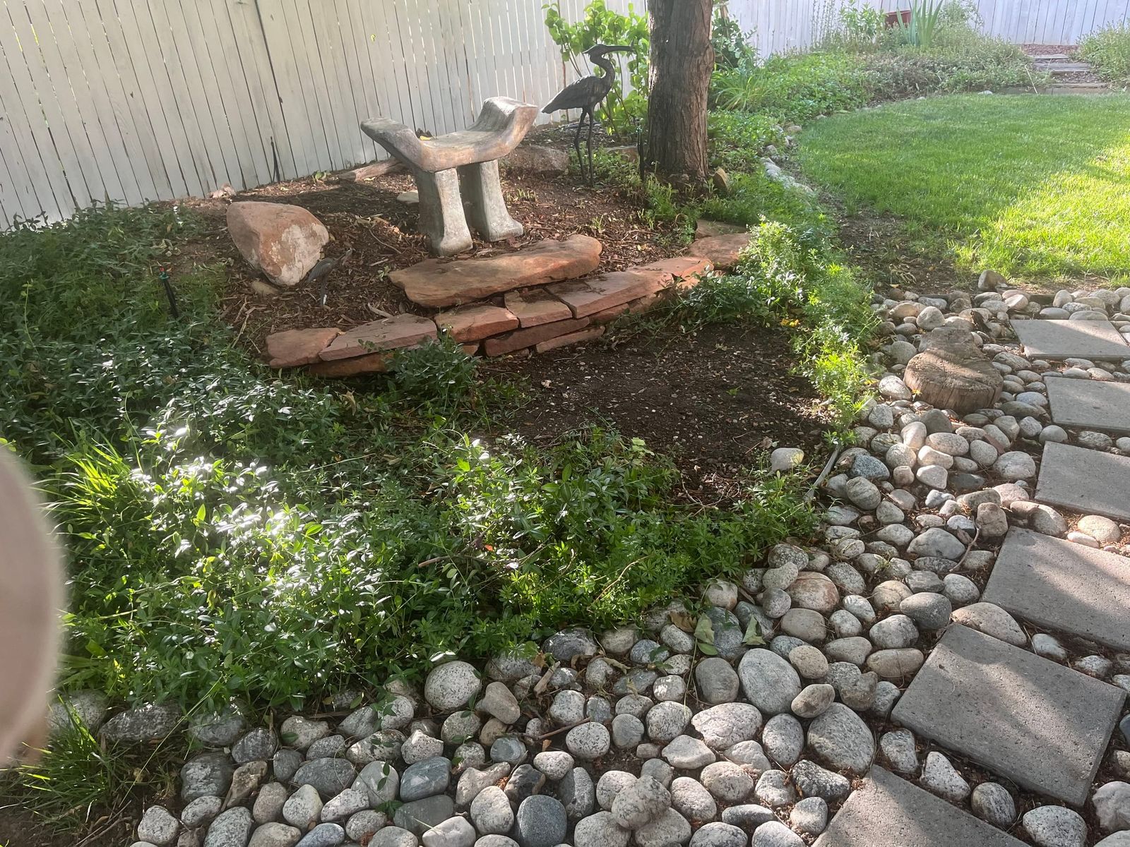 Circular garden bed with a stone bench, river-rock border and stepping pavers