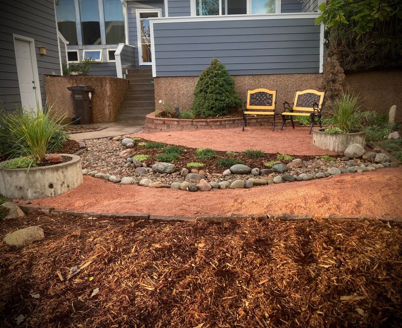 Backyard patio with chairs beside a curved river-rock bed and fresh mulch